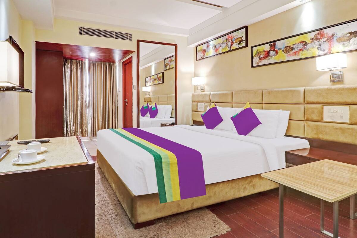 Quarto de hotel com cama, mesa de cabeceira e pequena escrivaninha com abajur.