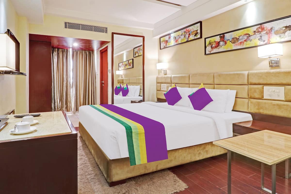 Una habitación de hotel con una cama, mesita de noche y un escritorio pequeño con una lámpara.