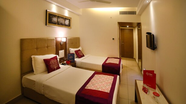 A hotel room with two beds, a ceiling fan, a TV, and a red sign on the nightstand. - Hotel Park N (Penumuluru)