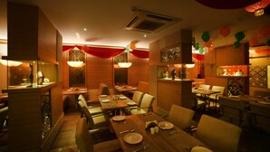 A restaurant with multiple dining tables and booths, red drapes, and decorative lighting. - Hotel Park N (Penumuluru)