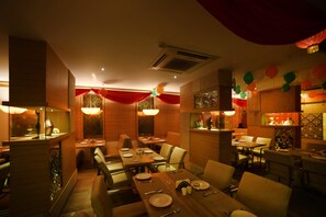 Un restaurant doté de nombreuses tables et de coins repas, de rideaux rouges et d’un éclairage décoratif.