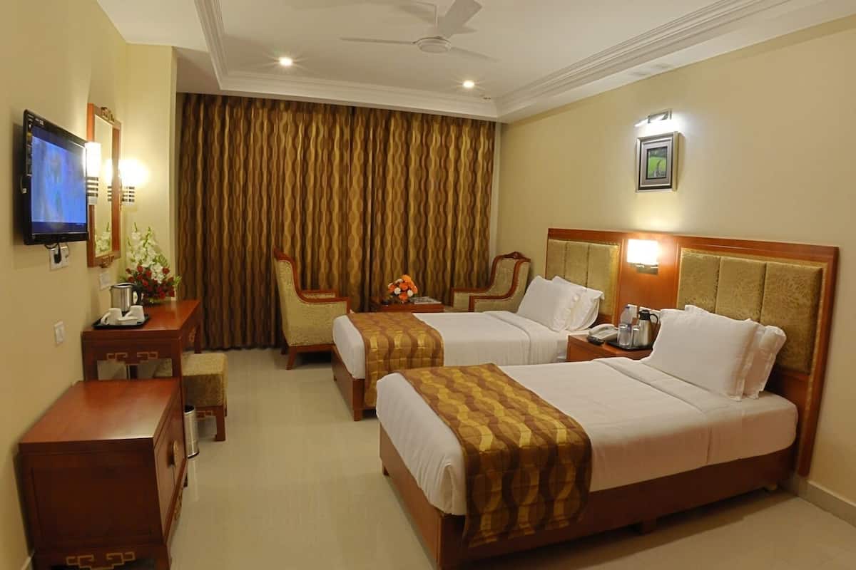 A hotel room with two beds, a TV, a desk with a lamp, and a chair.