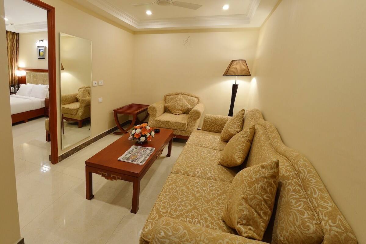 A hotel room with a bed, a sofa, a coffee table with flowers, a lamp, and a mirror.