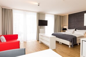 A modern hotel room with a bed, a red sofa, a white desk, and a TV. - eeeden apartments Graz (Graz)