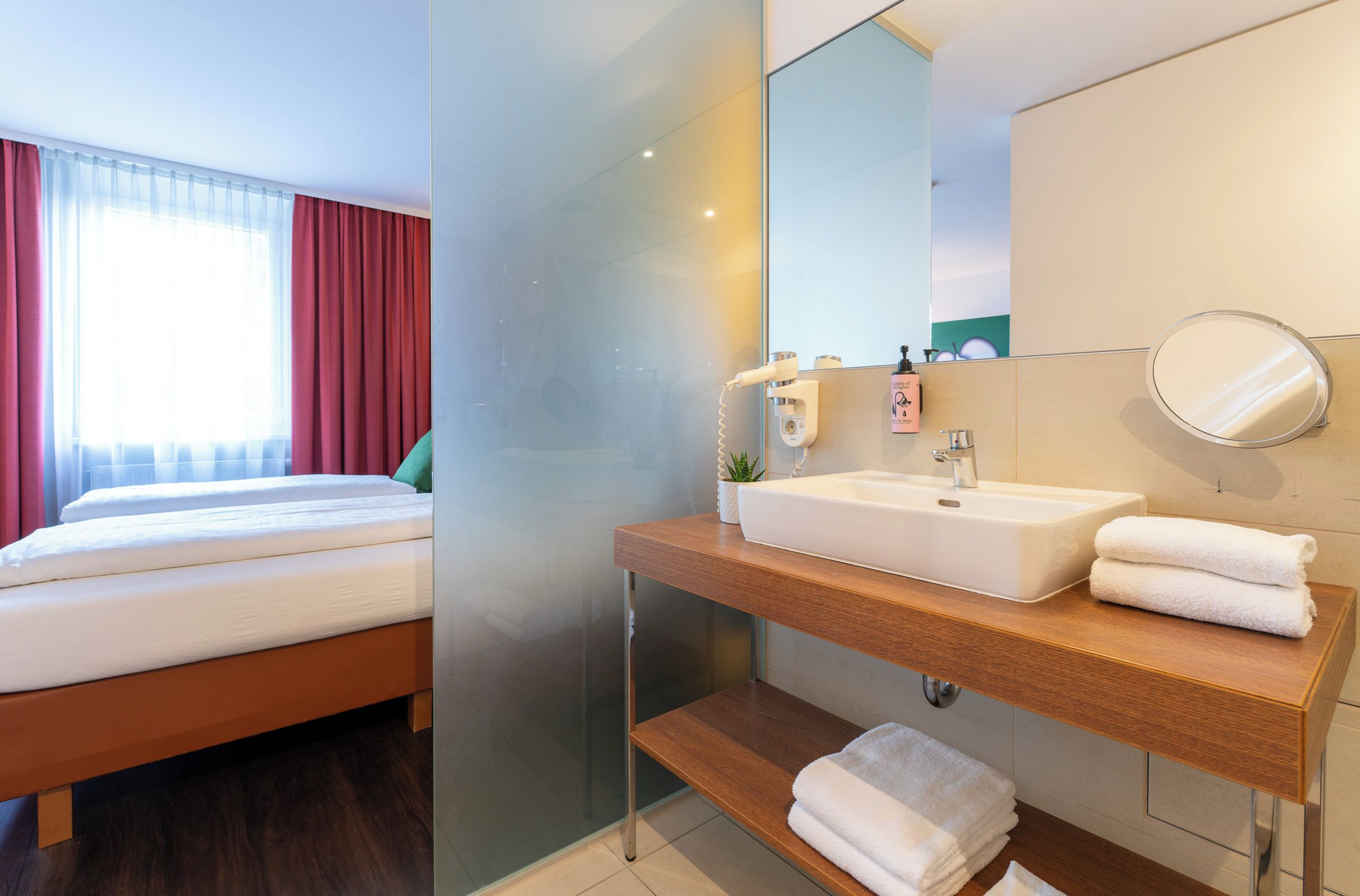 A hotel room with a bed, a bathroom with a sink, a mirror, and a towel.