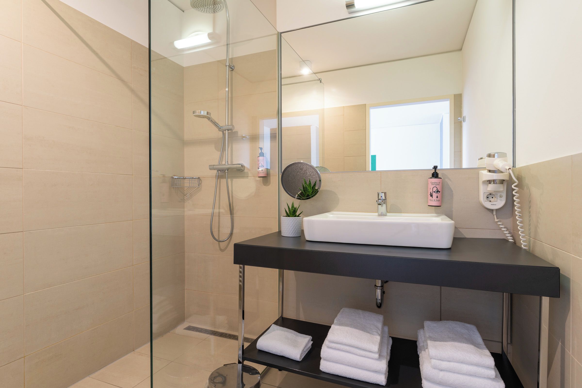 A modern bathroom with a glass-enclosed shower, a white sink, a black countertop, and a mirror.