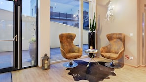 Un intérieur moderne avec deux fauteuils, une porte vitrée donnant sur l’extérieur, un cactus et une sculpture fixée au mur.