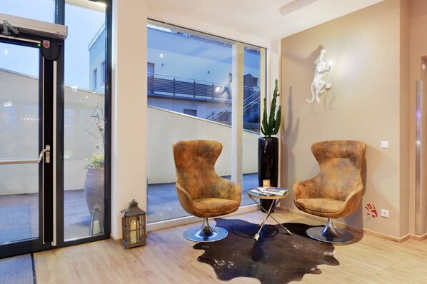 Un interior moderno con dos sillones, una puerta de cristal que da al exterior, una planta de cactus y una escultura en la pared.