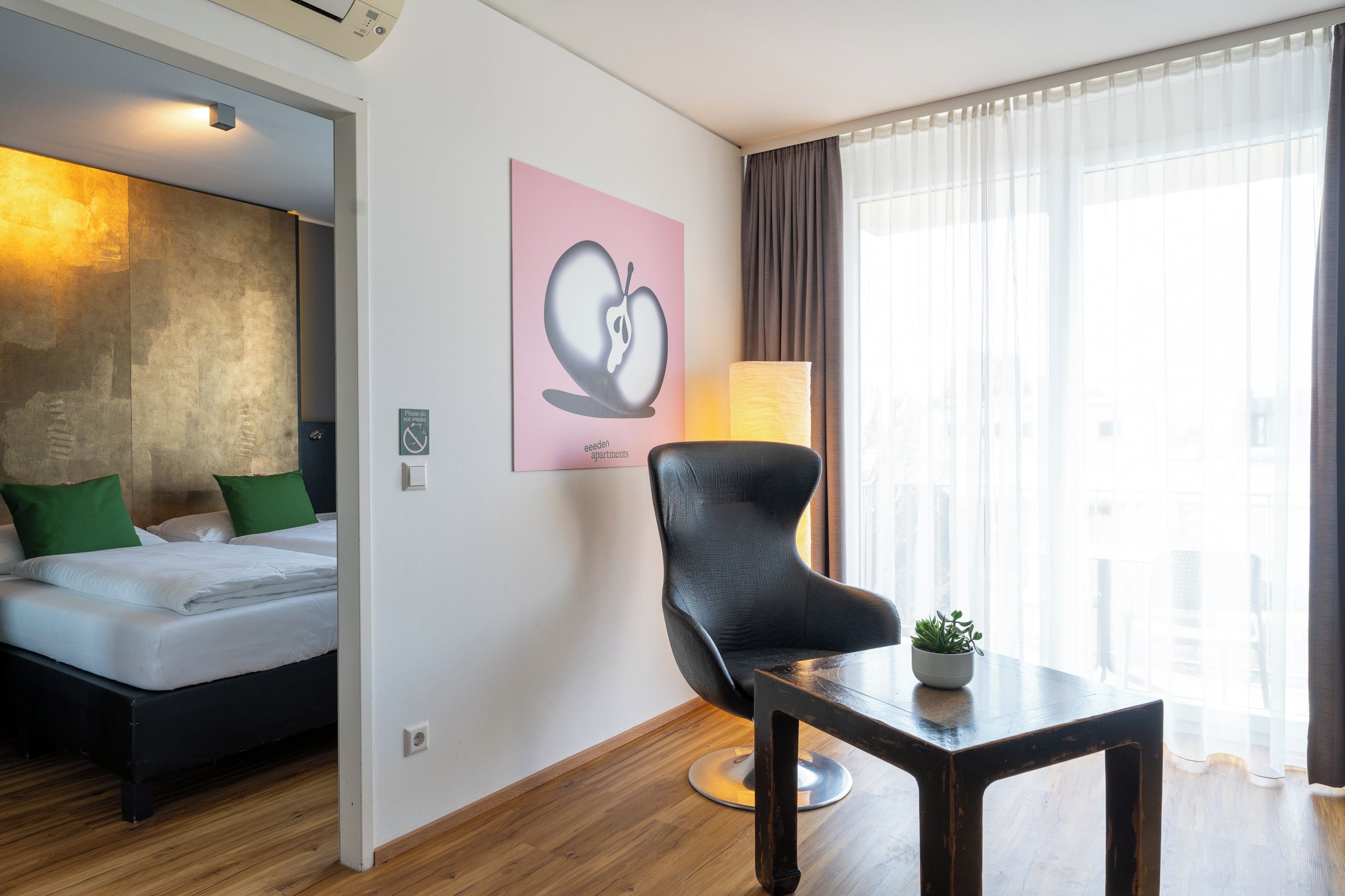 A hotel room with a bed, a chair, a table, a lamp, and a window with curtains.