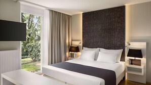 Une chambre d’hôtel moderne dotée d’un grand lit, de tables de chevet, d’un téléviseur à écran plat et offrant une vue sur la verdure environnante.
