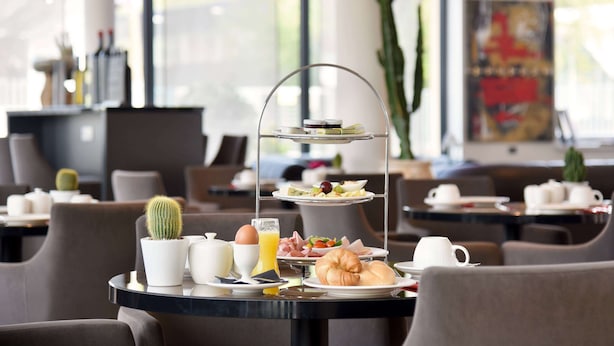 Une table mise pour le petit-déjeuner, avec un plateau à étages servant de présentoir, un cactus, un croissant et un verre de jus d’orange.
