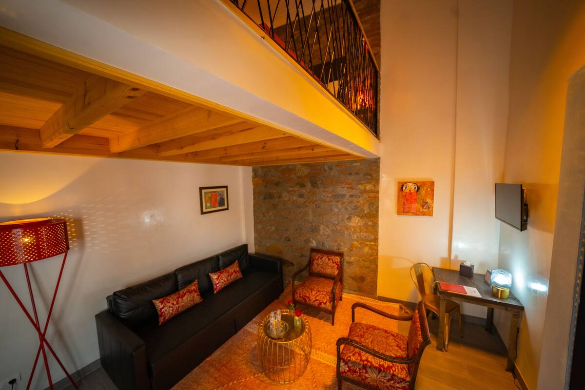 A cozy living room with a black sofa, patterned chairs, a wooden coffee table, and a stone wall.