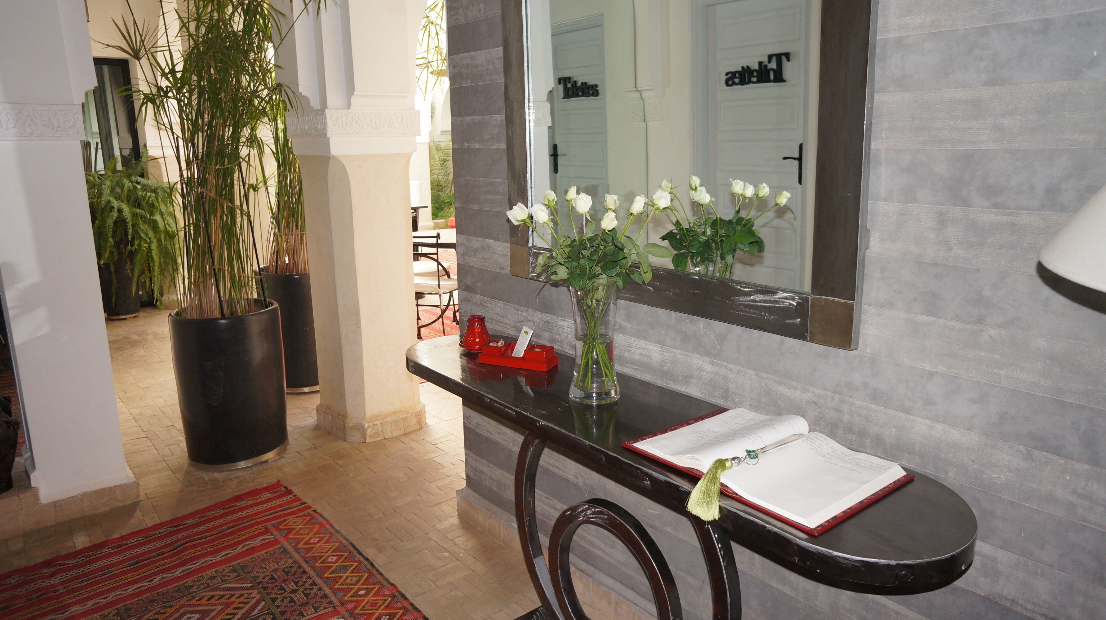 A reception area with a black console table, a vase with white flowers, a red tray, and a mirror on the wall.