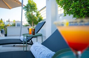 A sunlit outdoor seating area with lounge chairs and a table, a martini glass with a colorful drink, and a potted plant. - Riad Shanima & Spa (Marrakech)