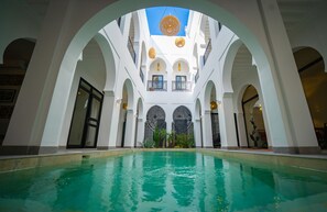 Zona de piscina amb una font central, envoltada d'arcs blancs i balcons amb seients a l'aire lliure.