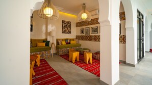 A spacious living area with a sofa set, wooden stools, and a red patterned rug. - Riad Shanima & Spa (Marrakech)