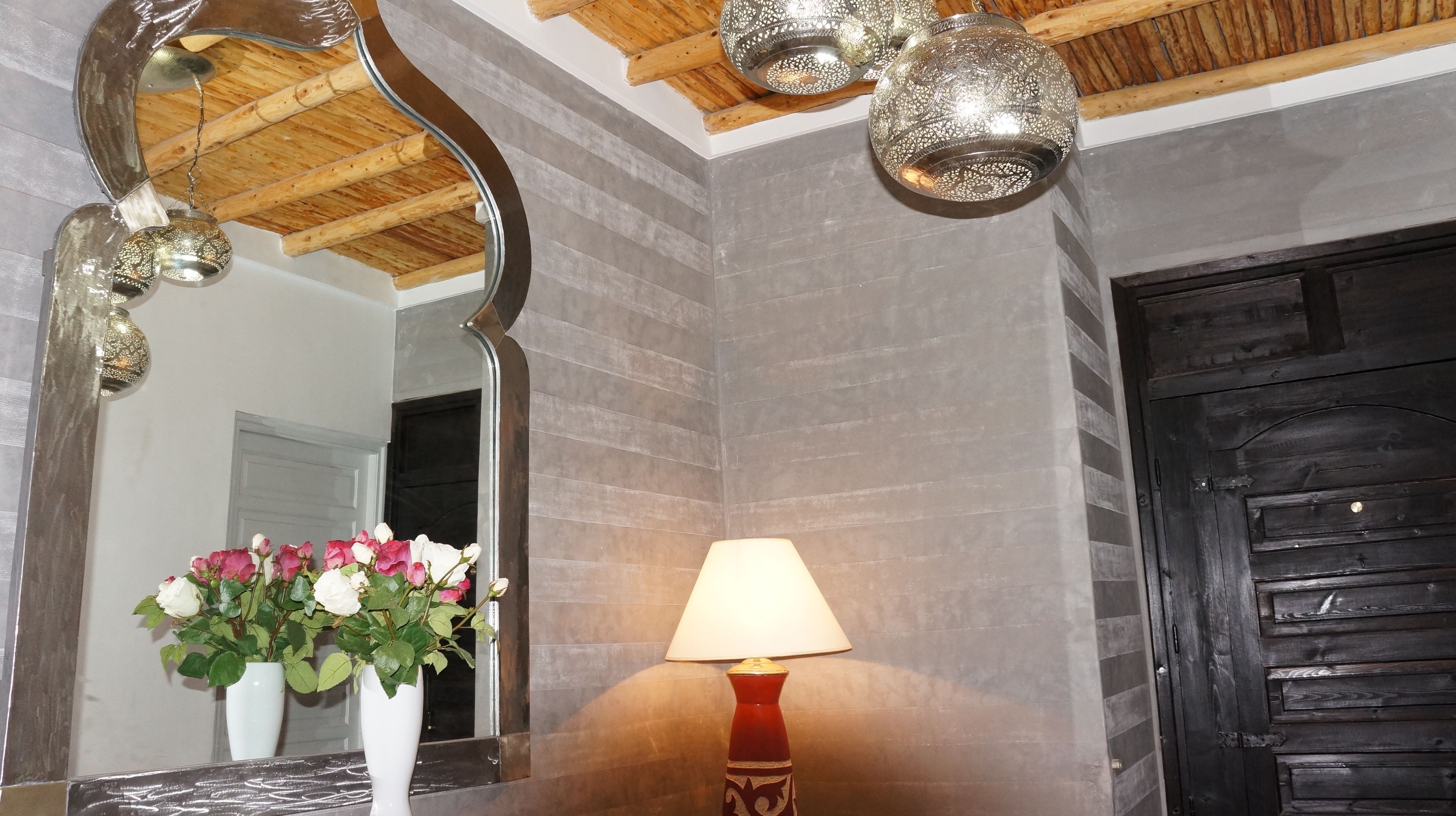 A bathroom with a large mirror, a vase of flowers, a lamp, and a wooden door.