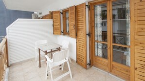 Un balcón con una mesa y sillas, contraventanas de madera y vista al interior.