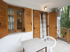Un balcón con contraventanas de madera, una mesa y dos sillas.
