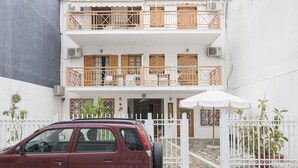 Un edificio de dos pisos con fachada blanca, balcones de madera y un coche estacionado al frente.