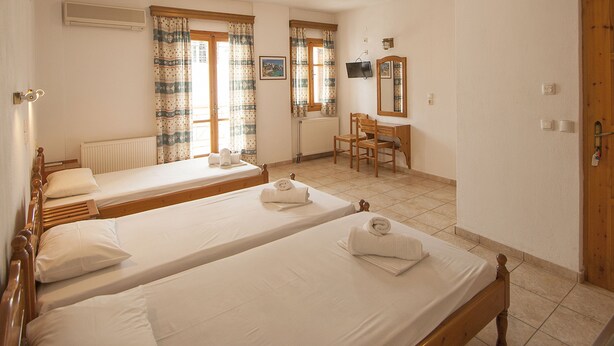 Habitación de hotel con dos camas individuales, un escritorio de madera, una silla, un radiador y un televisor en la pared.