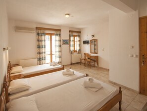 A hotel room with two single beds, a wooden desk, a chair, a radiator, and a television on the wall. - Pension Laura (Skiathos)