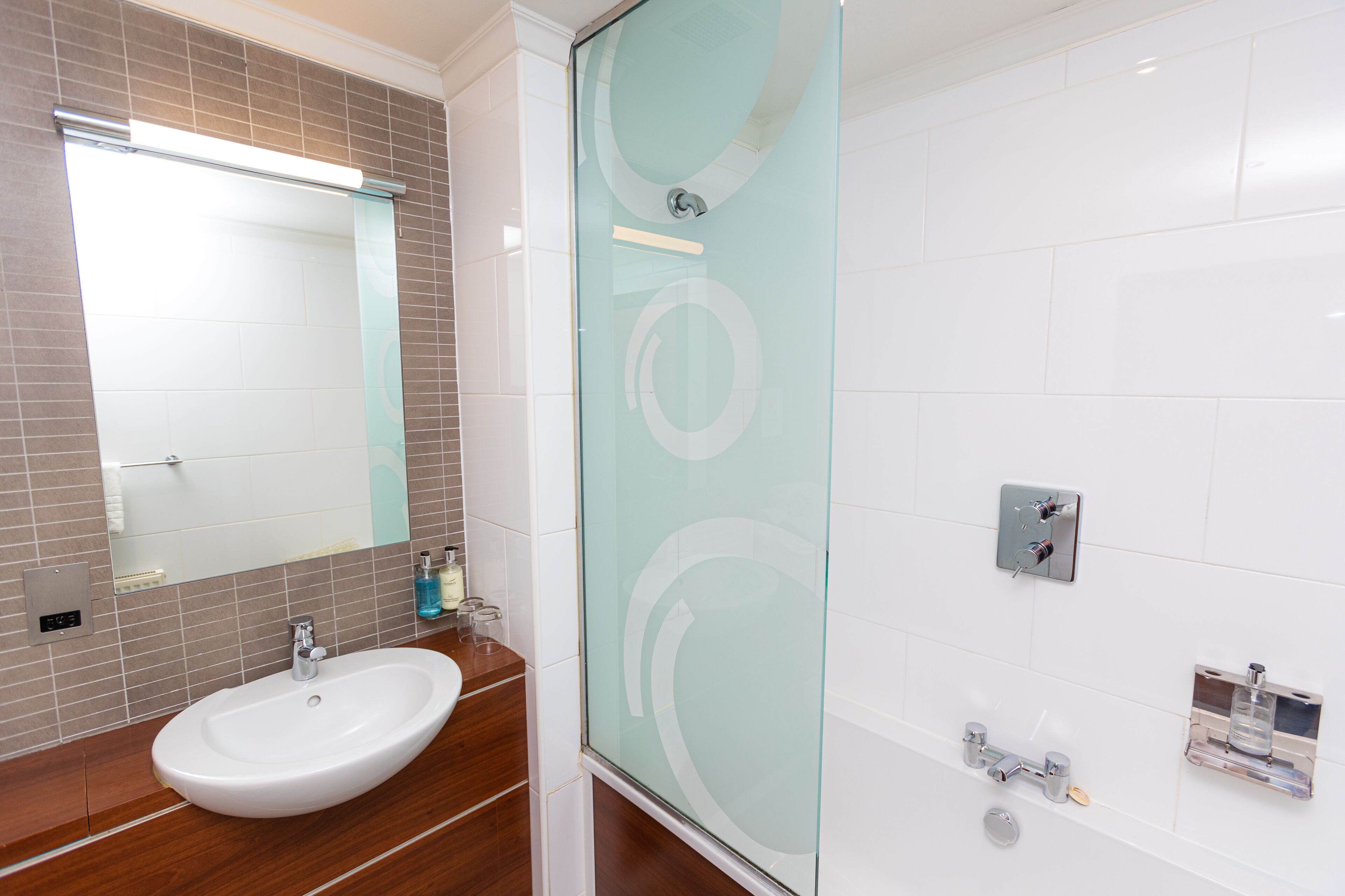 Un baño con lavamanos blanco, un espejo y una cabina de ducha de vidrio.