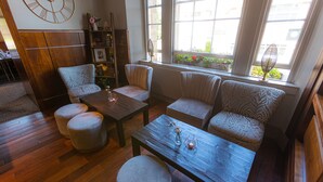 A cozy living room with a wooden floor, a large clock on the wall, and a window with plants. - Fletcher's Restaurant Bar & Rooms (Stirling)