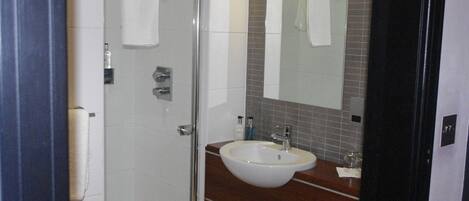 Un baño con mampara de vidrio, un lavabo blanco, un espejo y una toalla colgada en la puerta.