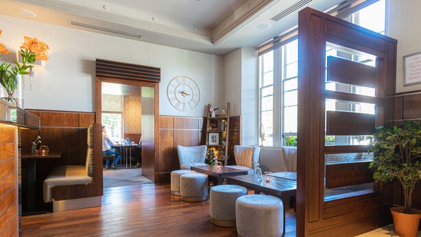 A modern lobby with wooden flooring, a seating area with ottomans, a clock on the wall, and a potted plant. - Fletcher's Restaurant Bar & Rooms (Stirling)