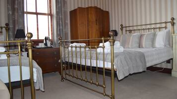 A bedroom with a four-poster bed, a wooden wardrobe, and a desk with a lamp.