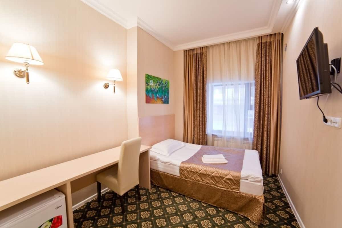 A hotel room with a bed, desk, chair, TV, and a painting on the wall.
