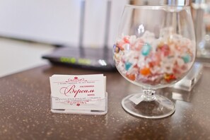 Tarjeta de presentación del Hotel Versha y un cuenco de vidrio lleno de caramelos de colores sobre una mesa.