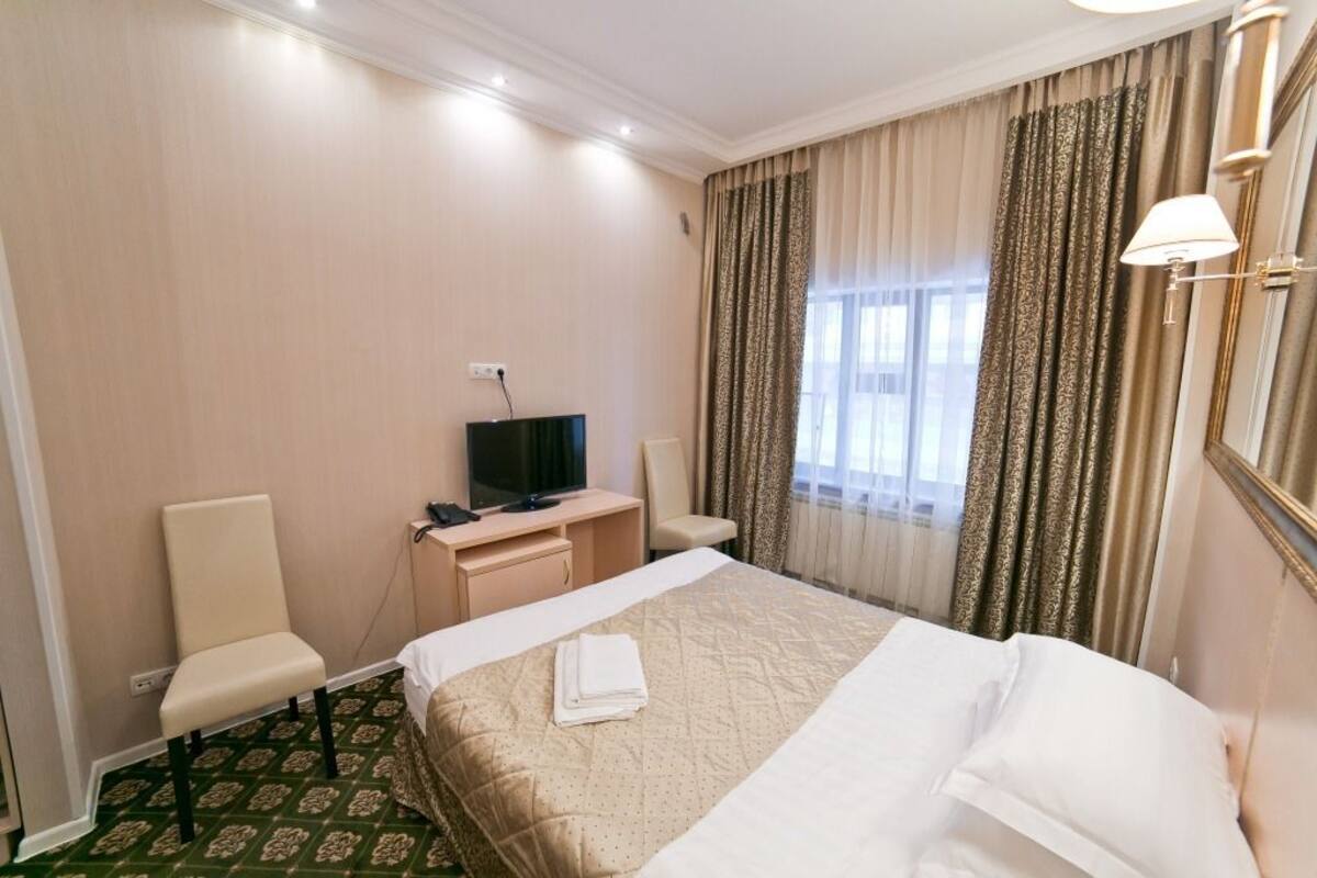 A hotel room with a bed, a desk with a television, a chair, and a window with curtains.