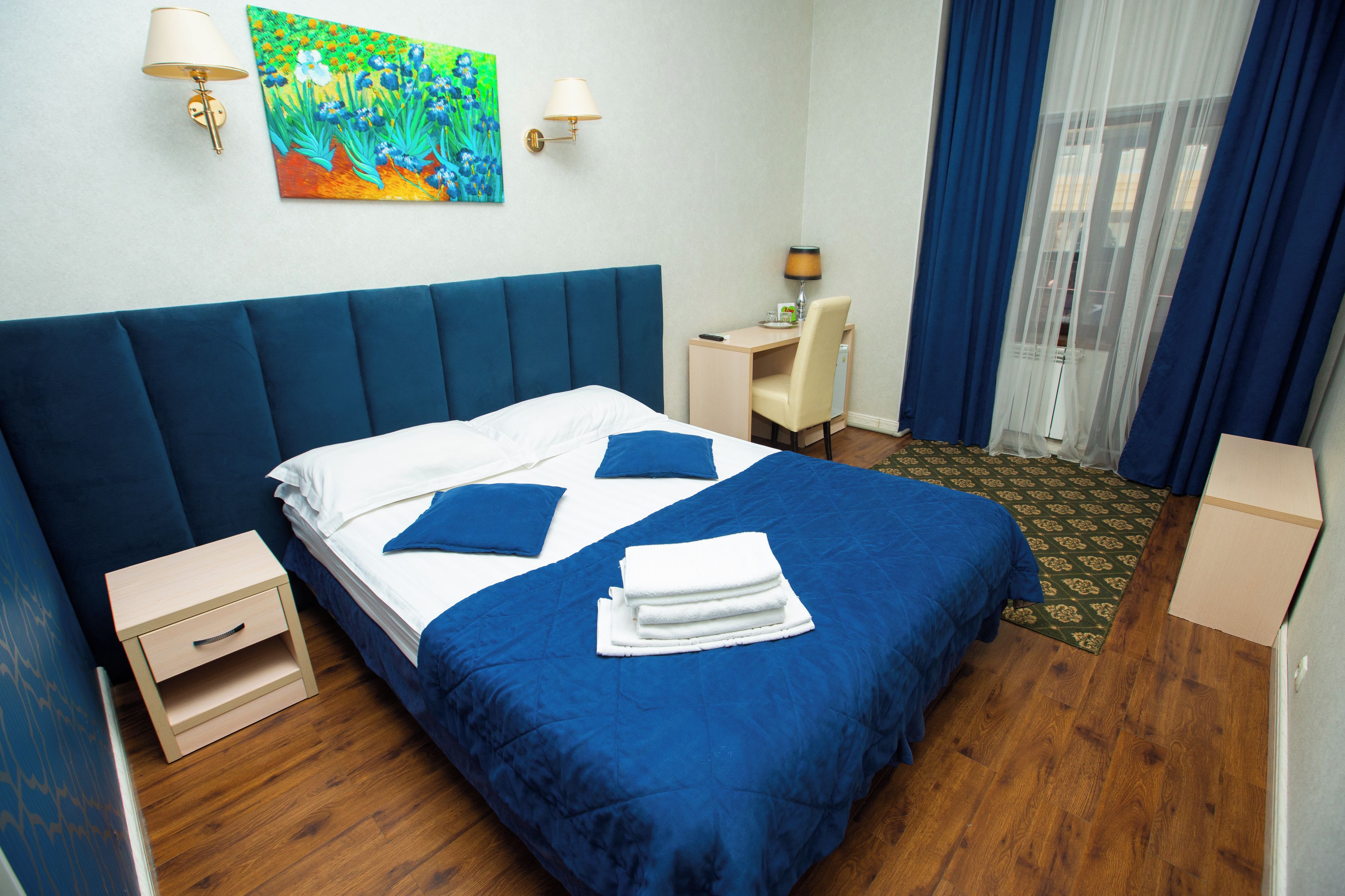 Quarto de hotel com uma cama grande, escrivaninha, cadeira, mesa pequena e um quadro na parede.