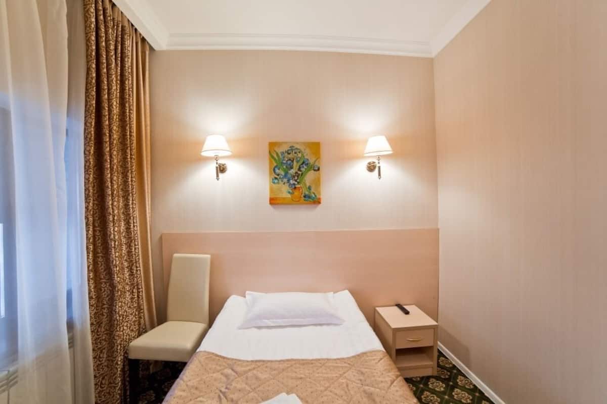 A hotel room with a bed, a chair, a nightstand, and two wall-mounted lamps.