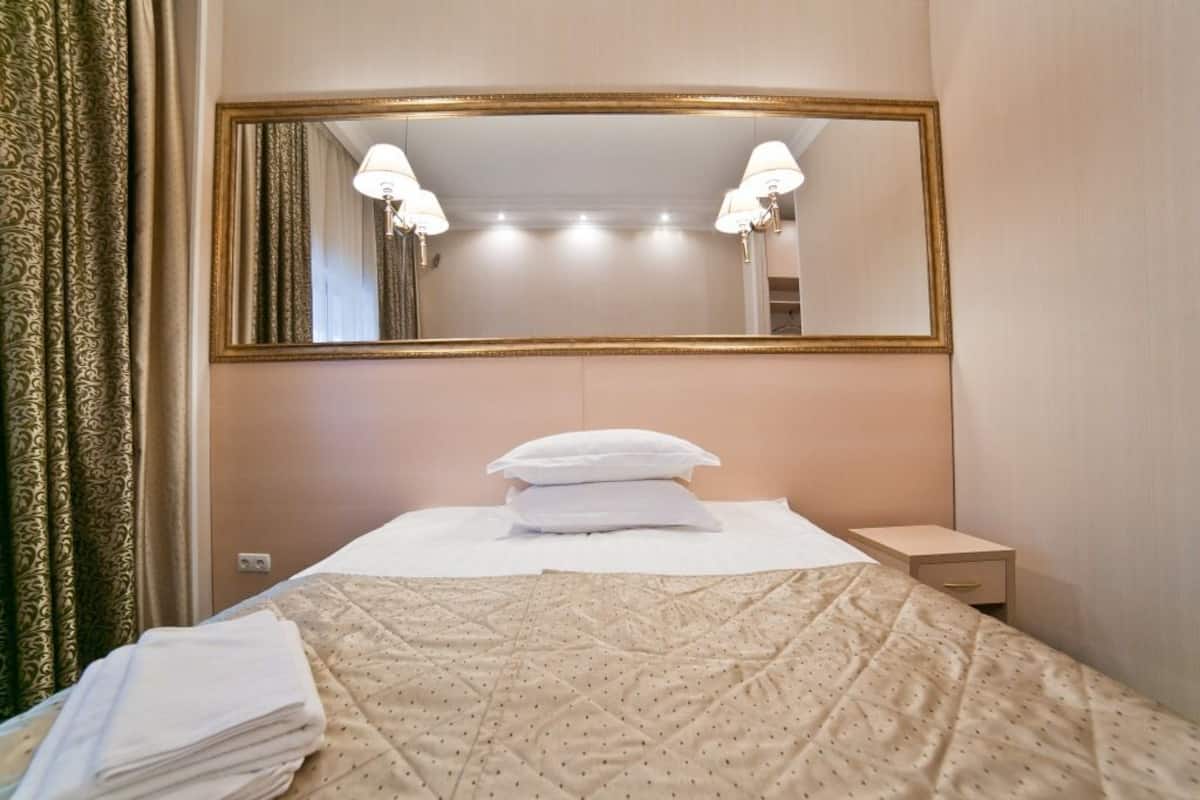 A hotel room with a bed, a large mirror, a nightstand, and a lamp.