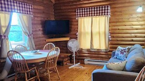 Un acogedor interior de cabaña con piso de madera, una mesa de comedor con sillas, un sofá y un televisor.
