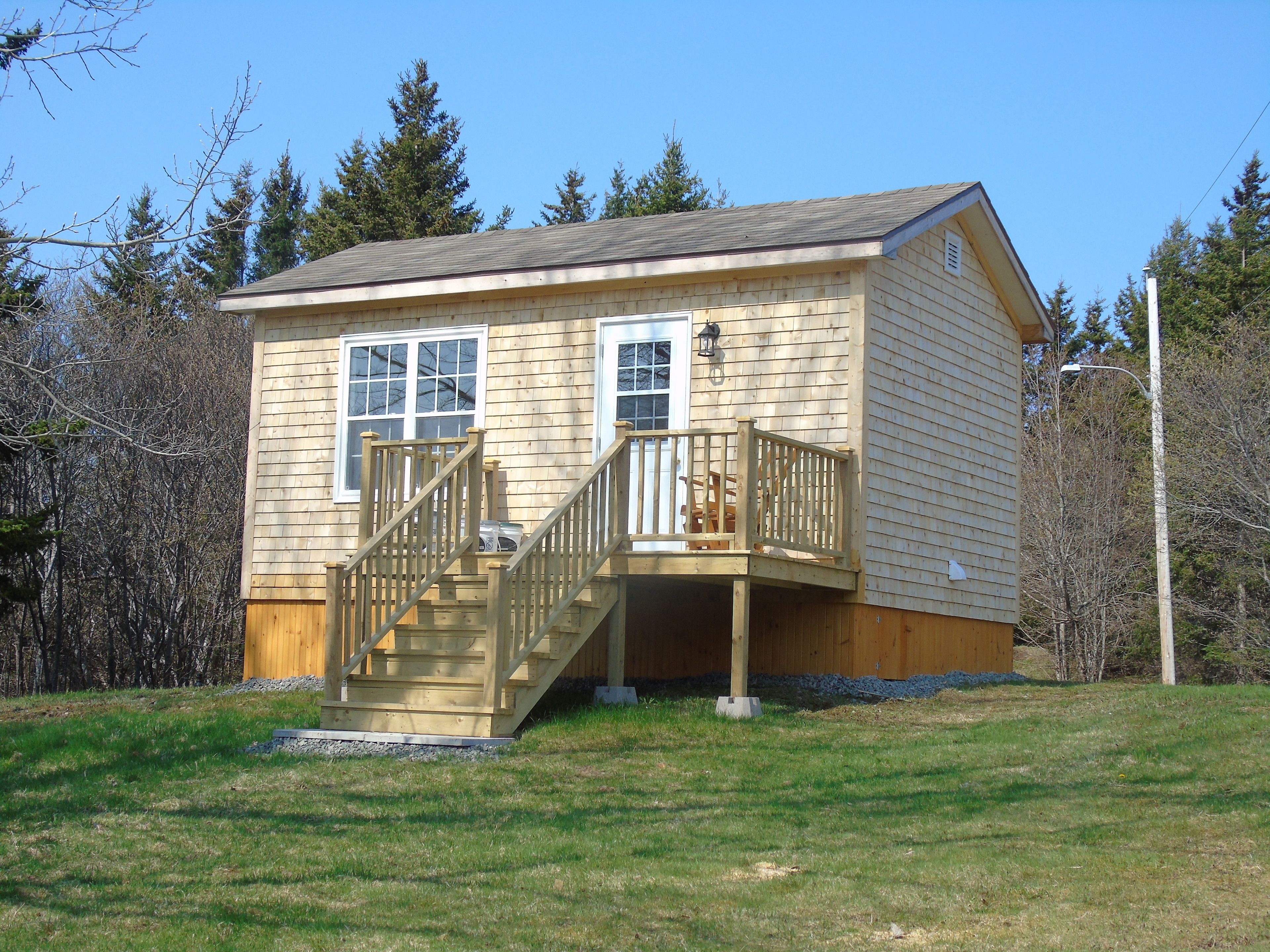 Une petite cabane en bois avec un porche à l’avant et un escalier menant à une terrasse.
