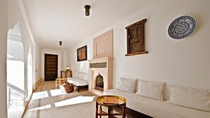 A spacious living room with a sofa, a small table, and a fireplace. - Riad Porte Royale (Marrakech)