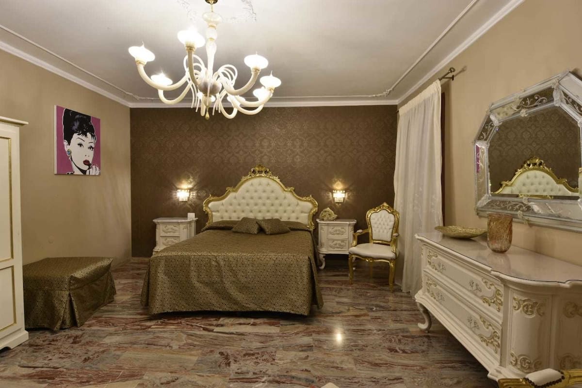A bedroom with a large bed, a chandelier, a dresser, and a mirror.