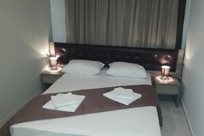 A neatly made bed with white linens and brown headboard, two bedside lamps, and a brown bedside table with a lamp. - Hotel Rex (Thessaloniki)