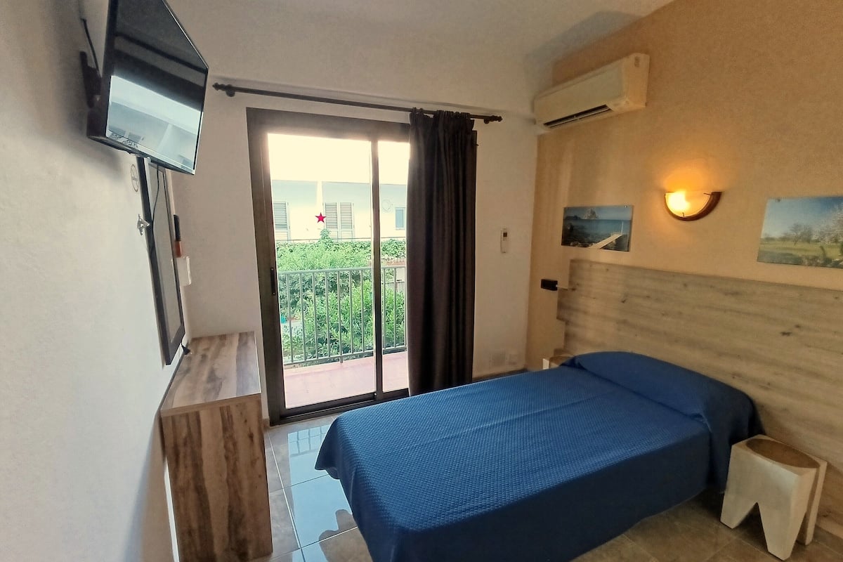 Une chambre d’hôtel équipée d’un lit, d’un téléviseur fixé au mur, d’un balcon avec vue et d’un appareil de climatisation.