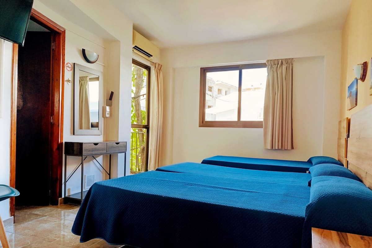 Une chambre d’hôtel avec deux lits, un bureau, un miroir et une fenêtre avec des rideaux.