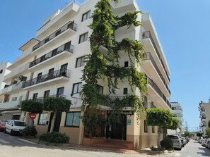 A multi-story building with balconies, a visible entrance, and parked cars along the street. - Hostal Horizonte (Sant Antoni de Portmany)