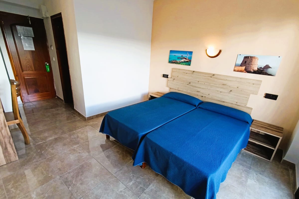 Une chambre à coucher comprenant un lit, une tête de lit en bois, une table de chevet, une lampe fixée au mur et deux tableaux encadrés.
