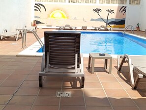 A poolside area with a lounge chair, a small table, and a mural depicting a beach scene. - Hostal Horizonte (Sant Antoni de Portmany)
