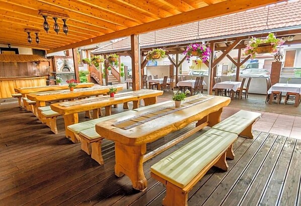 Une terrasse extérieure en bois, dotée de plusieurs tables de pique-nique et de bancs, et agrémentée de jardinières suspendues.
