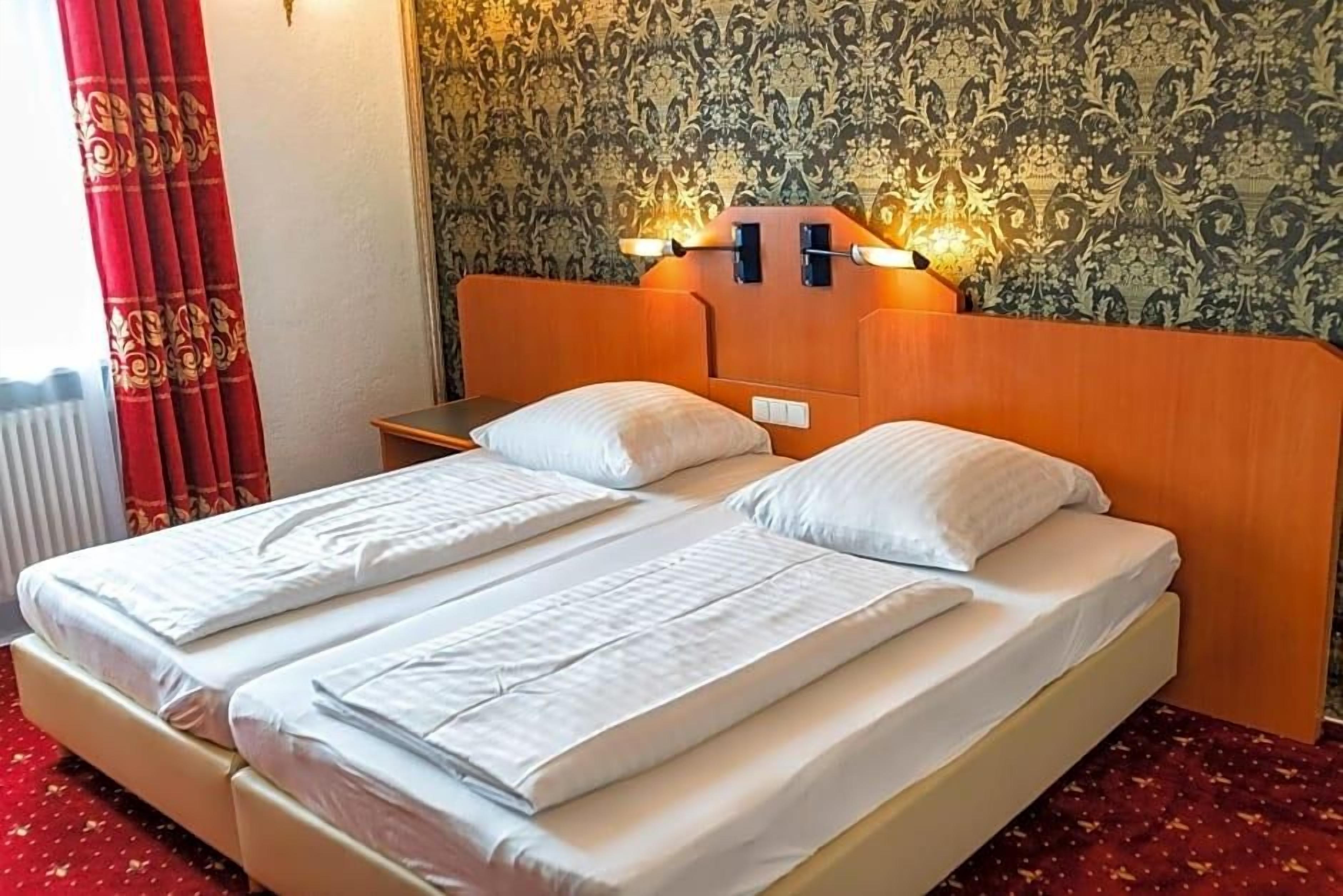 Un lit double avec une tête de lit en bois, deux tables de chevet et un papier peint à motifs.