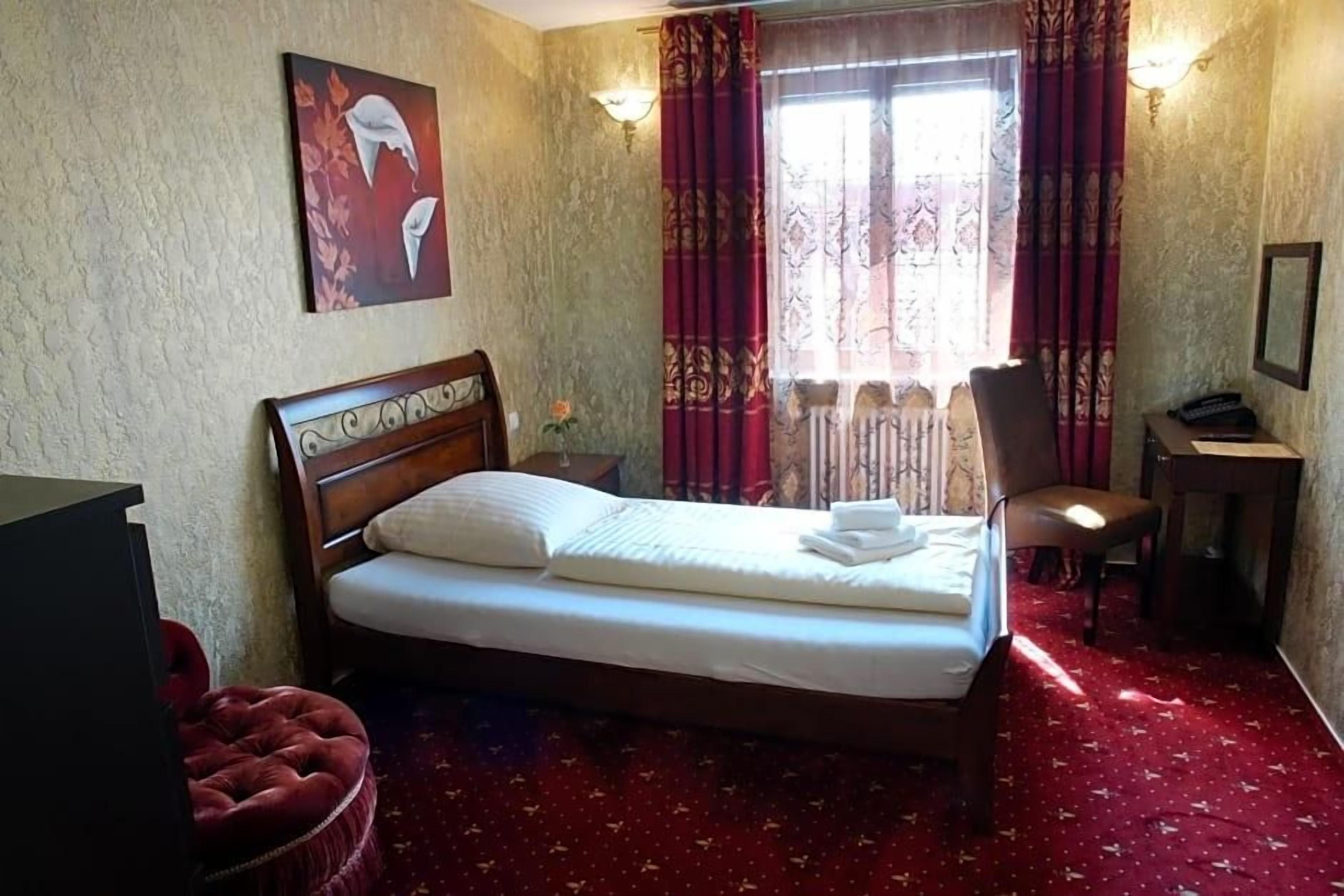 A hotel room with a bed, a chair, a desk, and a window with curtains.